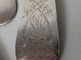 a silver spoon with a design on it next to a pair of silver spoons