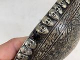 hand holding a silver bowl with skulls on it