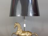 a gold horse lamp with a black shade on it