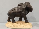 statue of two elephants standing on a sandy area with a light gray background