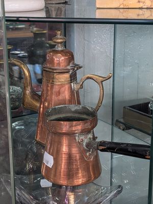 a glass case with a copper coffee pot on top of it