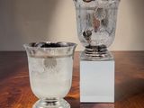 deux vases en argent posés sur une table en bois dotée d'un socle blanc