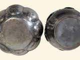 two silver dishes sitting on a white surface