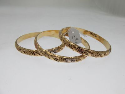 three gold bracelets with engraved designs on them on a white surface