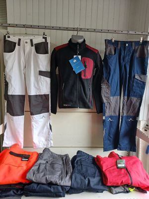 several pairs of pants and jackets hanging on a rack in a room
