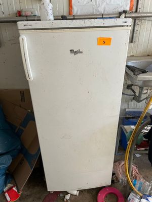 un réfrigérateur blanc posé dans un garage, à côté d'une pile de cartons