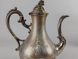 a silver tea pot with a handle and a handle on a stand