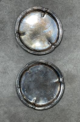 two silver plates sitting on a table with a black background