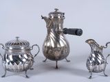 trois théières en argent et deux tasses en argent posées sur une table