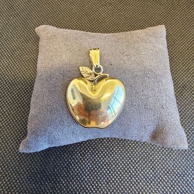 une photo d'un pendentif en forme de pomme en or posé sur un oreiller