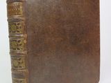 an old book with a brown leather cover sitting on a white surface