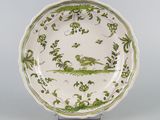 une assiette ancienne verte et blanche sur laquelle est représenté un oiseau
