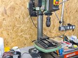 une perceuse posée sur un établi sur lequel se trouvent de nombreux outils