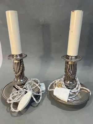 une paire de bougies plaquées argent, chacune posée sur un bougeoir blanc