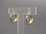 Boucles d'oreilles créoles bicolores or et argent, présentées sur un support en acrylique transparent