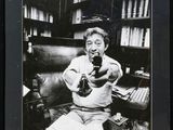 black and white photograph of a man sitting on a couch holding a camera