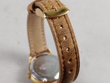 a close up of a watch on a white surface with a brown strap