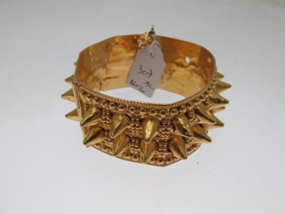 gold bracelet with spikes and a tag on it sitting on a white surface