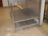 a stainless steel table with a shelf in the middle of the room