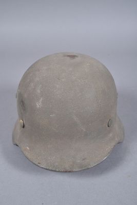 Un vieux casque repose sur une surface blanche, sur fond gris.