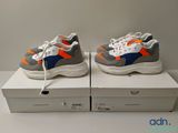 Deux paires de baskets sont posées sur des cartons, sur une table.