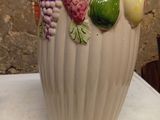 a white vase with fruit on it sitting on a table