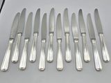six silverplated knives are lined up on a white surface