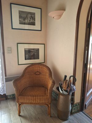 une chaise en osier dans un coin d'une pièce où sont accrochés des tableaux au mur