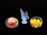 trois figurines en verre représentant des fleurs et un papillon sur fond noir