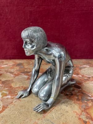 silver figurine of a woman crouching on a marble surface