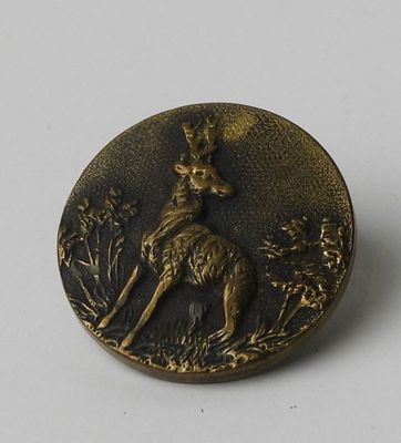 a bronze button with a deer on it on a white surface