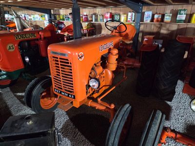 an orange tractor sitting in a barn with other tractors