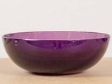 a purple bowl sitting on a table with a white wall in the background