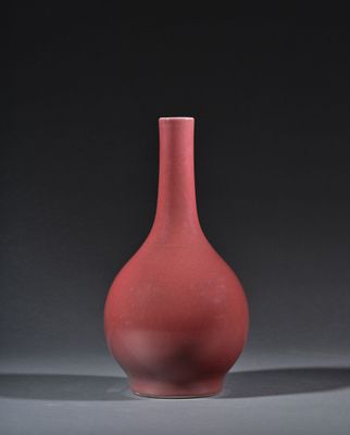 un vase rouge posé sur une table, sur fond noir