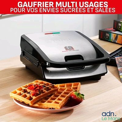 un gaufrier posé sur une table, avec une assiette de gaufres à côté