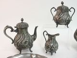 four pieces of silver tea set on display on a white surface