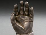bronze statue of a hand holding a small object on a white surface