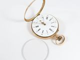 a gold pocket watch and a glass on a white surface
