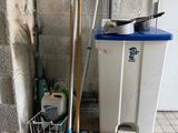 a trash can with brooms and a mop next to a trash can