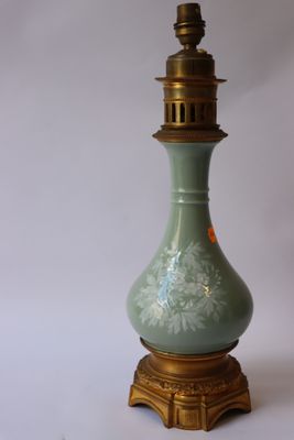 un vase vert posé sur un socle doré, sur fond blanc