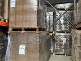 des cartons empilés sur des palettes dans un entrepôt, avec un homme debout à côté d'eux