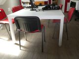 une table blanche avec des chaises rouges et un ordinateur posé dessus