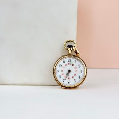 une petite montre de poche en or posée sur une table blanche