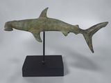 a bronze shark sculpture on a black stand on a white background