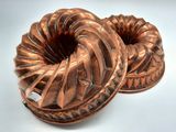 une paire de moules à gâteau Bundt en cuivre ancien sur fond blanc