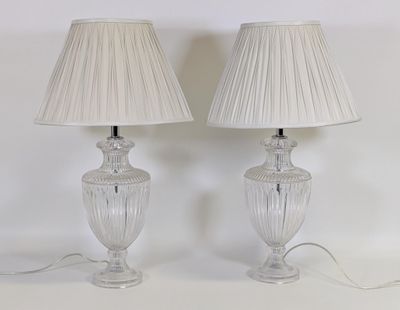 une paire de lampes en verre transparent avec des abat-jours en plis, posées sur un support blanc