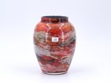 un vase rouge avec un couvercle noir posé sur une surface blanche