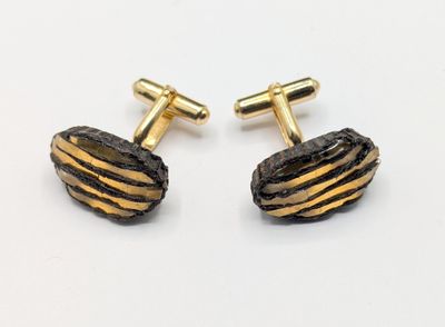 two pairs of gold and black striped cufflinks on a white surface