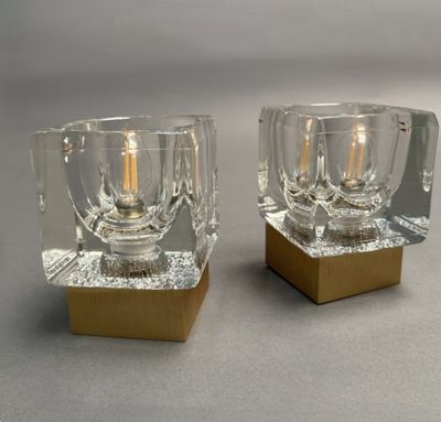 paire de bougeoirs en verre transparent avec des socles dorés, posés sur un support gris