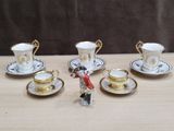 cinq tasses et soucoupes posées sur une table, avec une figurine représentant un homme